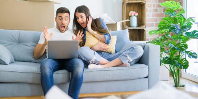Young beautiful couple relaxing sitting on the sofa of new house using computer laptop very happy and excited, winner expression celebrating victory screaming with big smile and raised hands